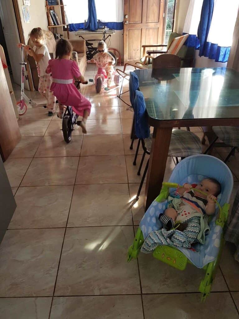 children riding bike and scooter in small house and baby in rocker
