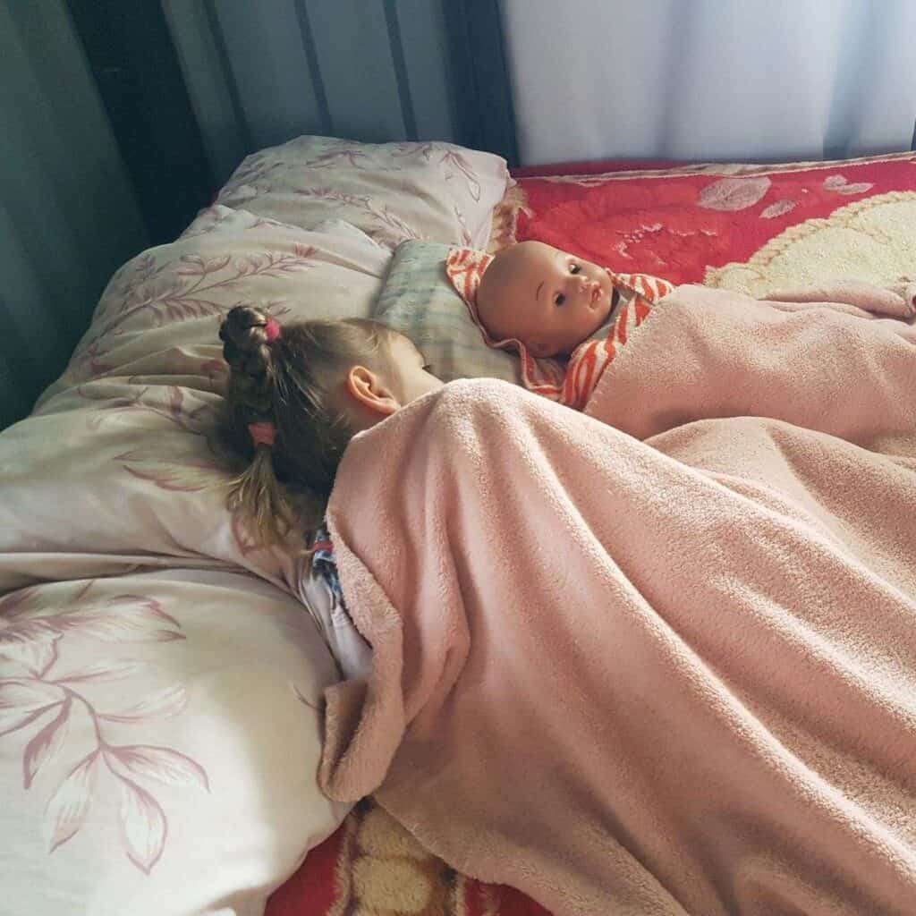 girl resting in bed with doll