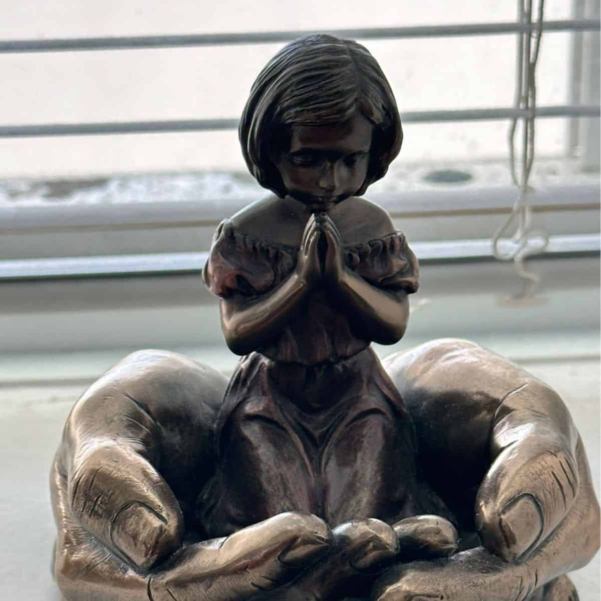 figurine of girl praying in God's hands